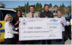 Outdoor image of smiling people all helping to hold a large check